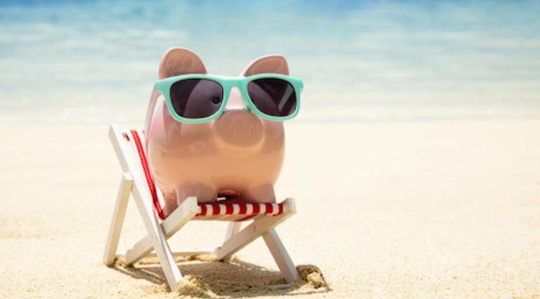 Cochon tirelire posé sur un transat avec des lunettes de soleil sur une plage